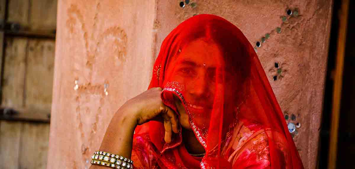 An Indian woman from rural India in veil or ghunghat, wearing bright coloured attire, Rajasthani Village life.