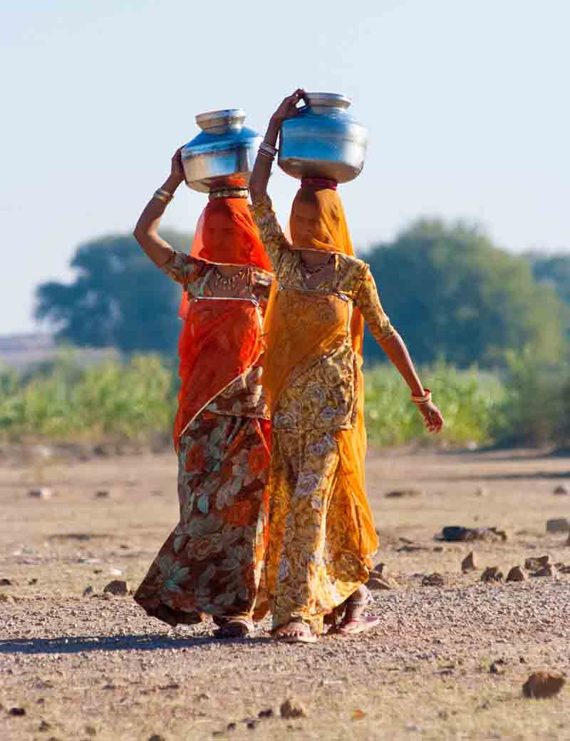Colourfully dressed Rajasthani women carrying water pots on their heads in rural villages of Rajasthan.