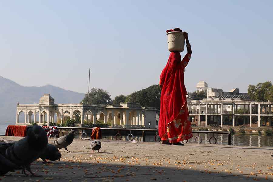 A Young Traditional village woman carrying water on her head in a bucket, moving on the ghats of lake pichola
